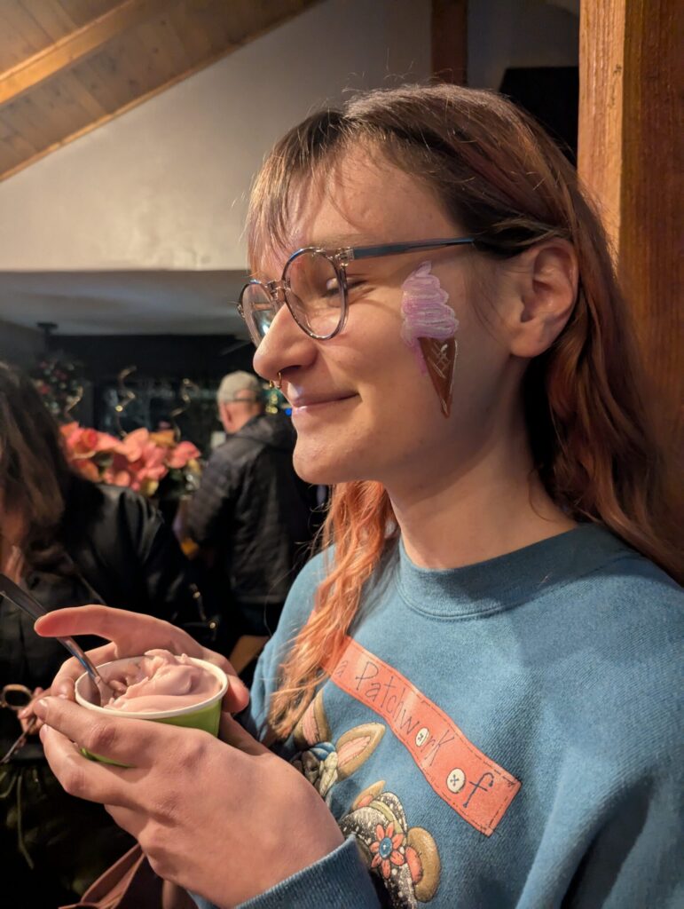 A customer with an ice cream cone on their cheek from face painting and a cup of Ripple Soft Ice Cream cupped in their hands!